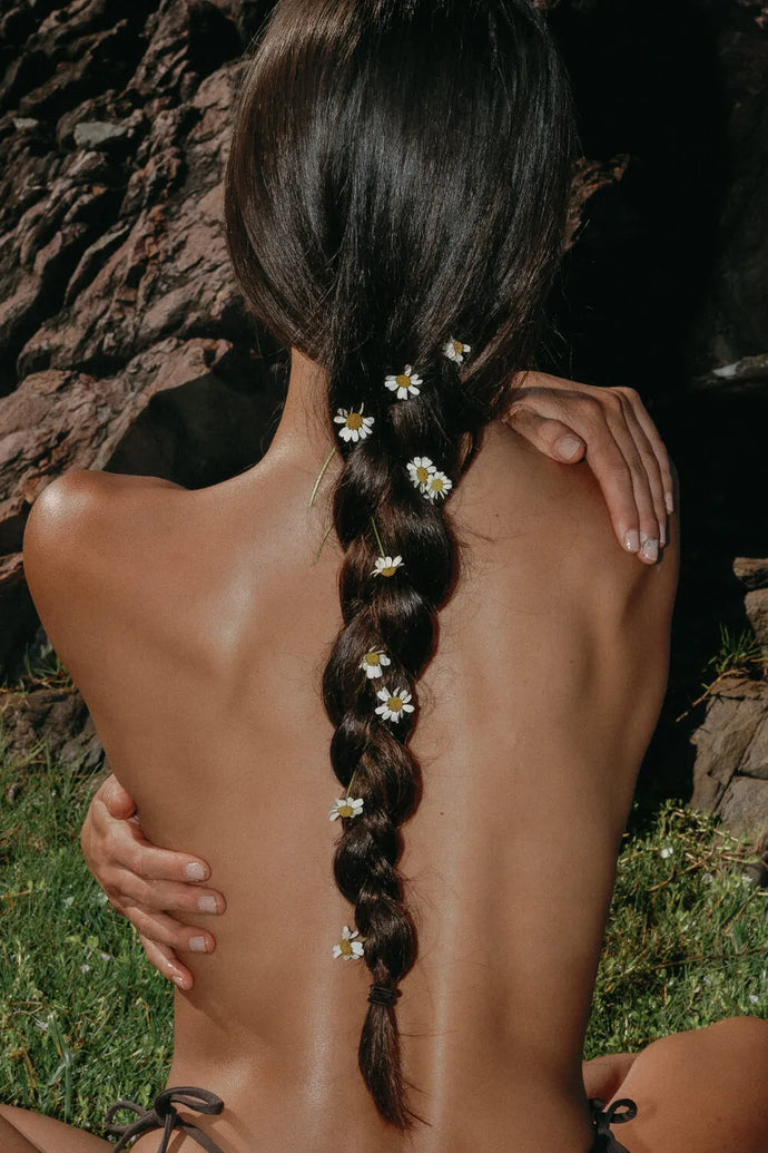 Vrouw van achteren met bloemen in het haar – natuurlijke schoonheid en zachtheid, beeld dat linkt naar het merkverhaal van Mamé Care.